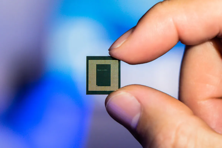 Close-up of a hand holding a Qualcomm chip, showcasing its intricate design and small size.