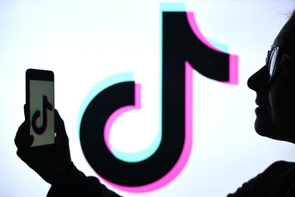 A person holding a phone with the TikTok logo on its screen, silhouetted against a large, vibrant TikTok logo in the background.