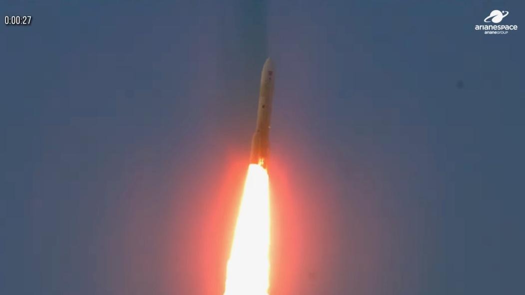 The Ariane 6 rocket ascending into the sky, with powerful flames from its engines visible against the clear blue backdrop, during its successful launch.