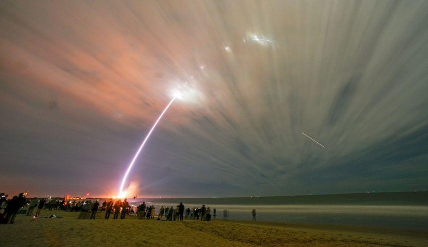 Historic Mars mission and Jeff Bezos’ New Glenn rocket’s major debut postponed due to weather 2 Spectacular launch of a rocket into the sky, captured from a beach as onlookers watch the ascent against a backdrop of clouds and vibrant colors.