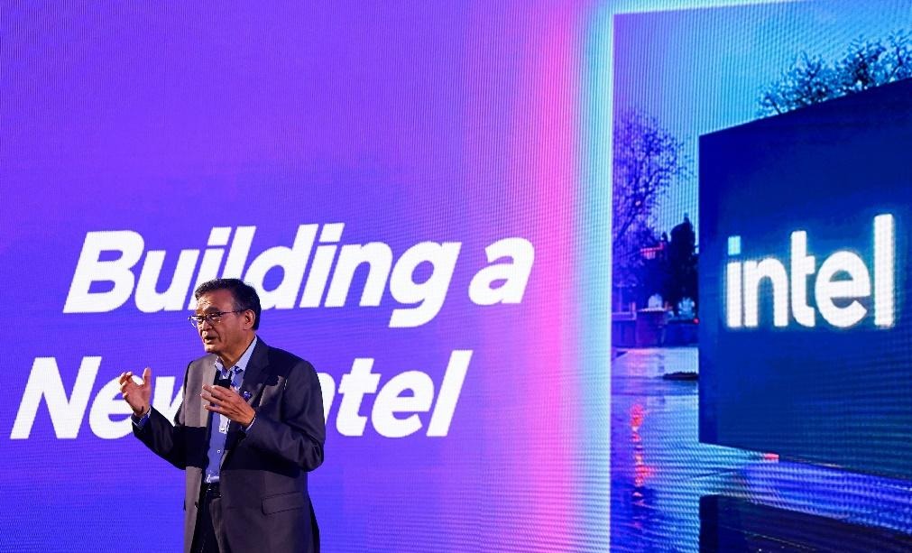 Intel CEO Lip-Bu Tan speaking at an event with a large screen in the background displaying the words 'Building a New Intel' and the Intel logo.