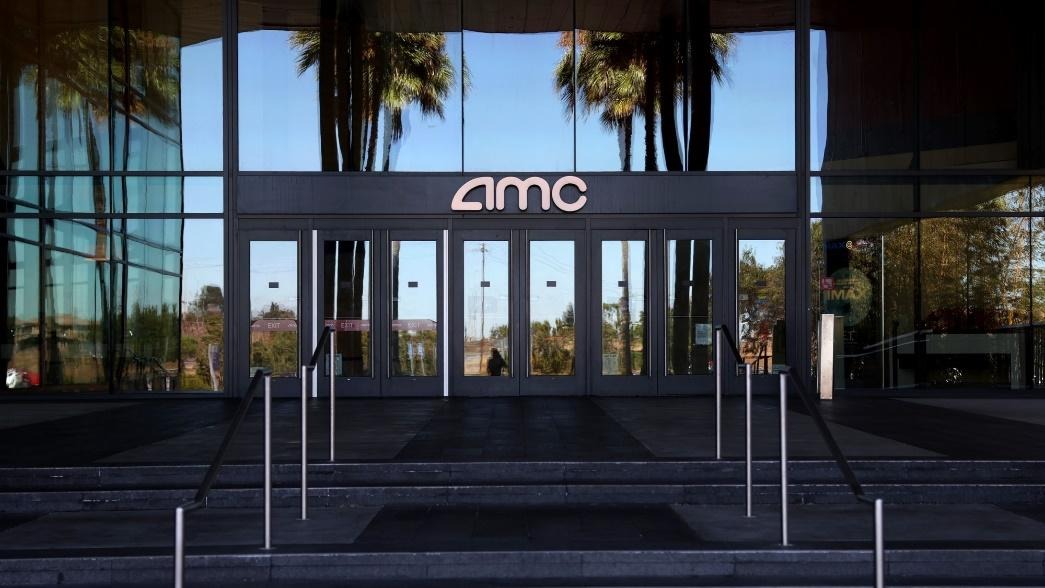 AMC Shuts Down Three Theaters in Illinois Here’s Which Ones Closed and Which Locations are Still Open 1 Entrance of an AMC theater showcasing the company’s logo on the glass doors with reflections of palm trees in the background.